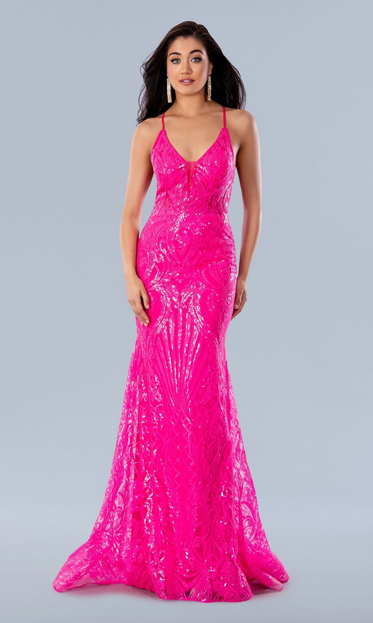 A woman stands against a light gray background wearing the Sheer-Waist Long Sequin-Print Prom Dress 24115, a bright pink, floor-length gown with a fitted sequin bodice, flared skirt, and strappy back design.